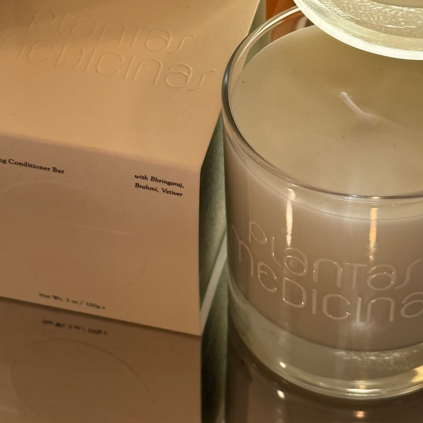Glass jar with 'plantas medicinas' branding next to a cardboard box on a reflective surface.