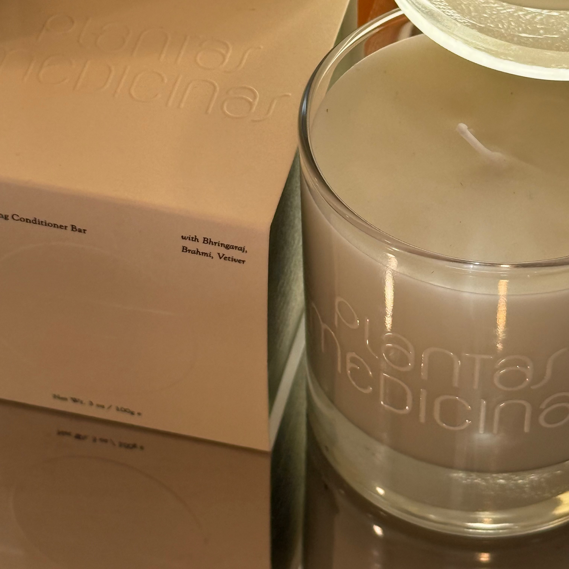 Glass jar with 'plantas medicinas' branding next to a cardboard box on a reflective surface.